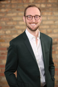 Cory-Rothschild-Headshot trẻ chuyên nghiệp đeo kính và trang phục công sở