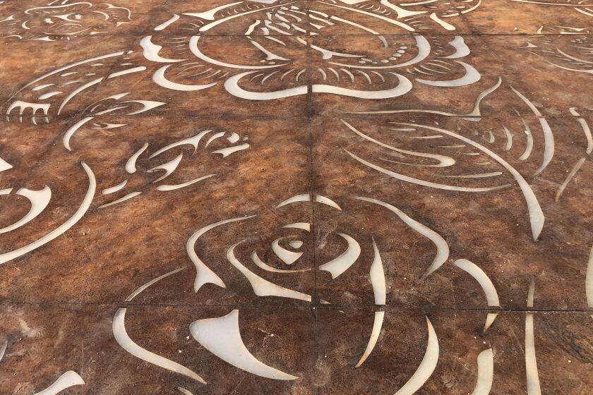 Una vista detallada de la placa de acero Corten colocada en el suelo muestra contornos de rosas y un par de manos en oración