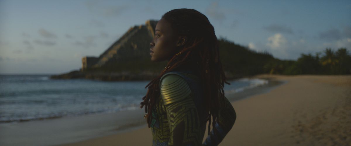 Lupita Nyong’O as Nakia, standing on a beach looking out towards the ocean in Black Panther: Wakanda Forever.