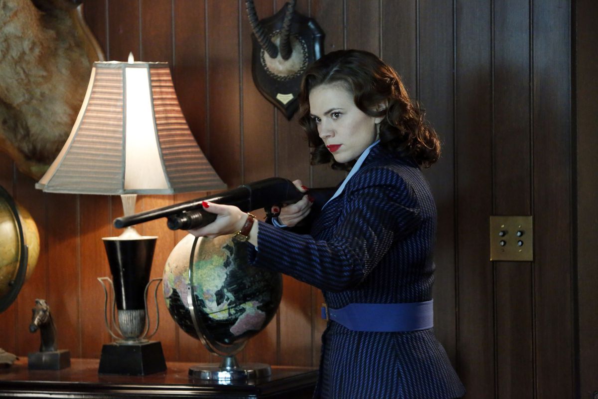 Agent Carter holds up a shotgun in someone’s wood den