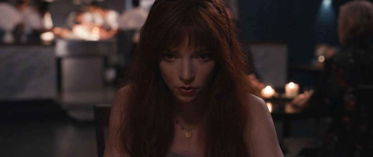 Margo (Anya Taylor-Joy), una mujer con un vestido que deja al descubierto los hombros y una espesa cabellera roja, mira fijamente a la cámara en primer plano en The Menu.