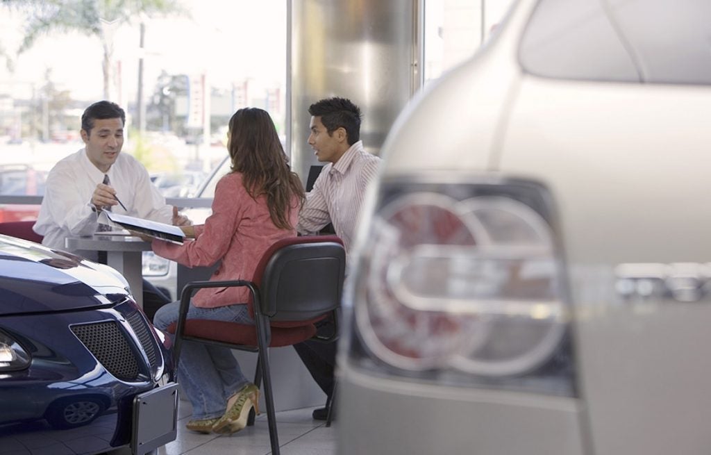 Salesman and couple sitting at desk in car showroom, focus on background
