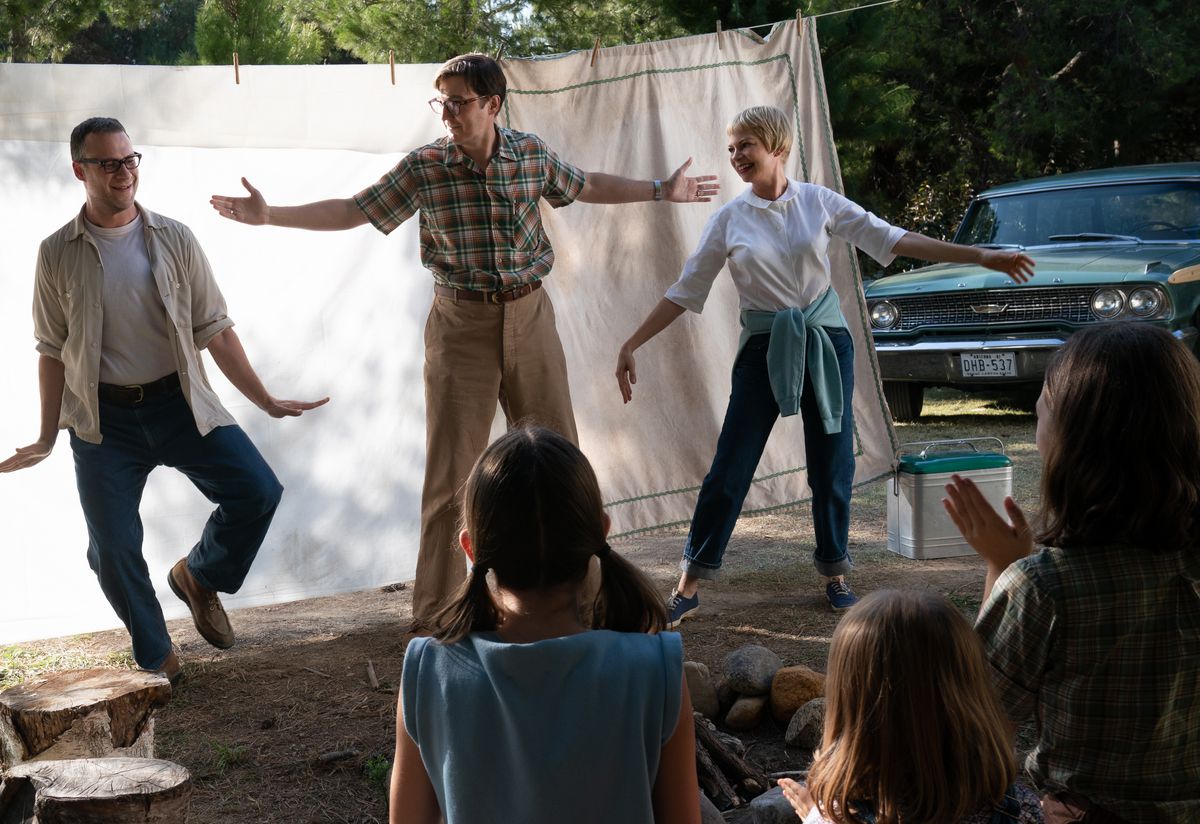 Bennie Loewy (Seth Rogen), Burt Fabelman (Paul Dano), and Mitzi Fabelman (Michelle Williams), cavort in front of a white, hanging bedsheet backdrop as several people with their backs to the camera watch in The Fabelmans