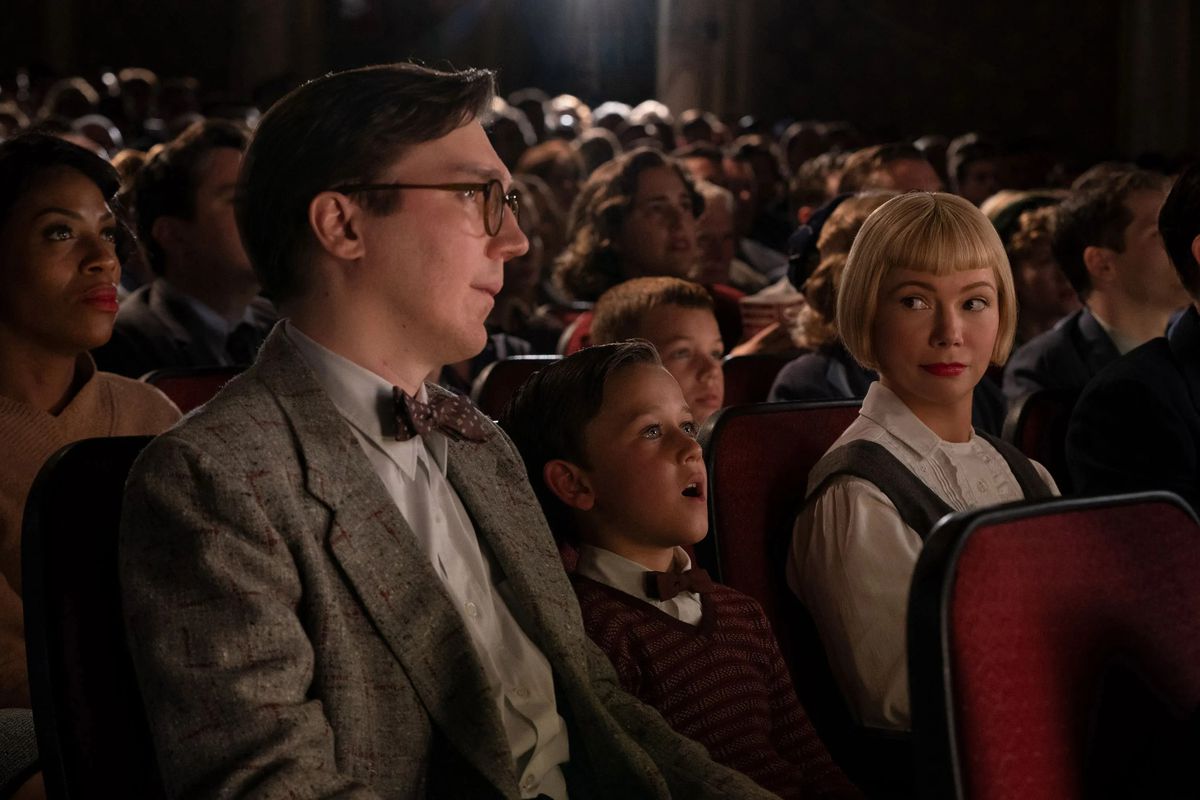 Young Sammy (Mateo Zoryon Francis-DeFord) gapes in wonder at the movies, sitting between his father Burt (Paul Dano) and mother Mitzi (Michelle Williams), who share a knowing smile over his head in The Fabelmans