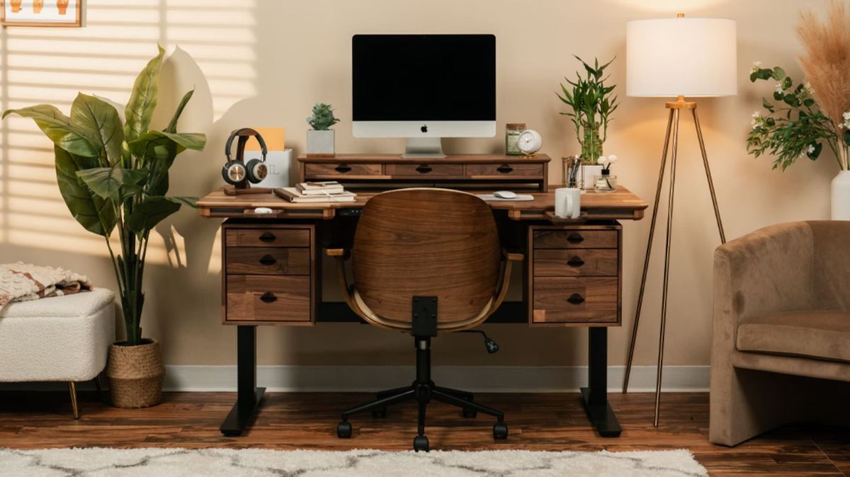 El núcleo del escritorio modular Wyrmwood es un marco negro. La superficie aquí es de nogal oscuro, con dos cubículos cada uno con tres cajones. Un topper de escritorio sostiene un monitor, mientras que un accesorio magnético sostiene una taza de café.
