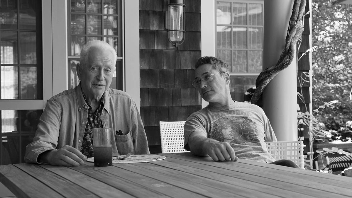 Robert Downey Jr. regarde avec amour son père alors qu'ils sont assis à une table dans une image en noir et blanc.