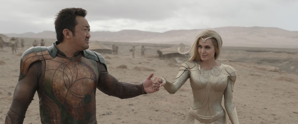gilgamesh, a burly asian man, holds a hand out to the ethereal thena, a blonde woman in all white