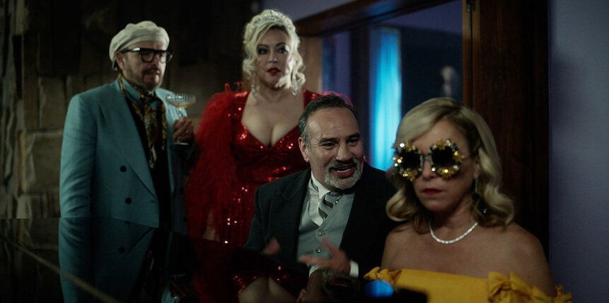 Four people, including Jennifer Tilly and Joe Pantoliano, gather around a piano in fancy dress in Chucky.