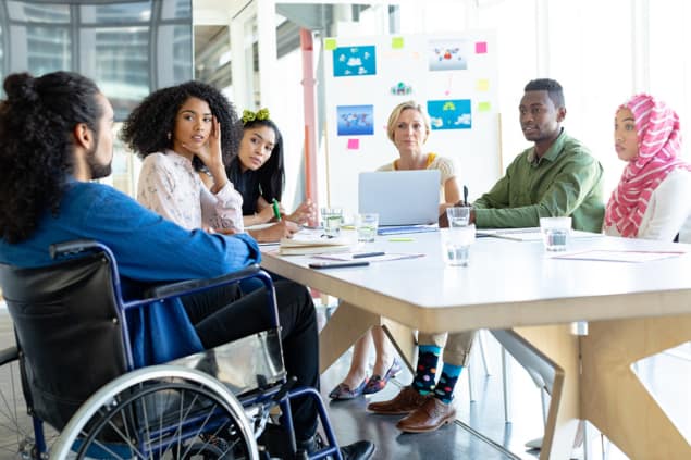 Conference table in an office with several people sat around it, including a wheelchair user