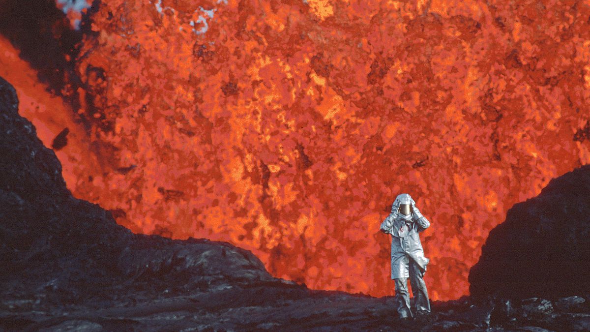 Een persoon in een vuurvast pak loopt weg van de monding van een geiser die overloopt van lava.
