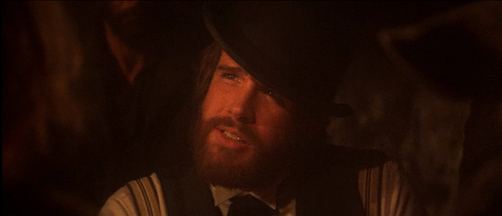 Een close-up van een bebaarde man (Warren Beatty) met een bolhoed.