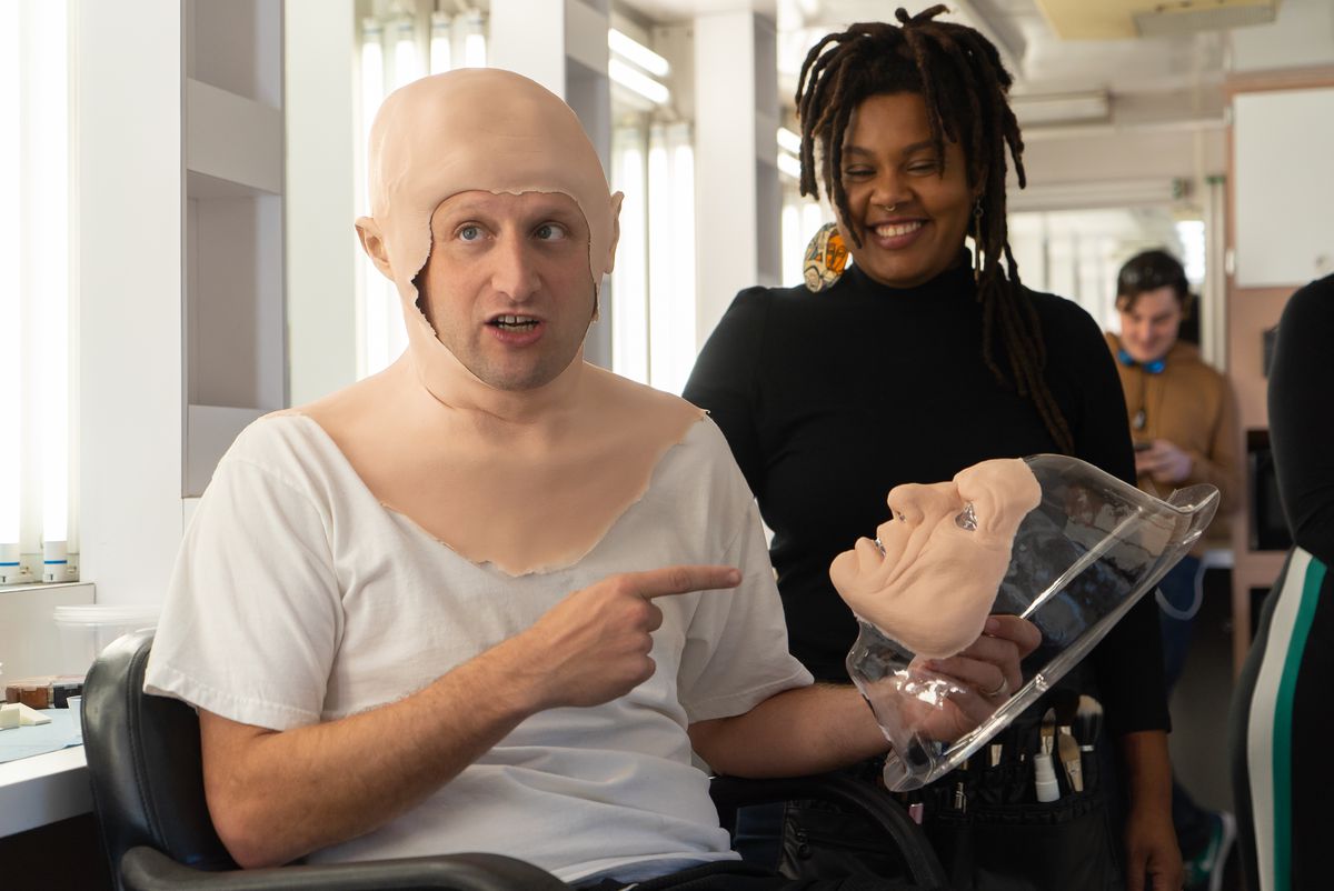 A still of I Think You Should Leave as Tim Robinson wearing prosthetics and holding the mask to go over his face.