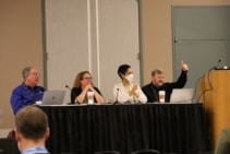 Фотография Билла Тигпена, Дженнифер Отт, Чайри Баттон и Марка Фернандеса, сидящих за столом во время панельной дискуссии. Фернандес показывает большой палец вверх