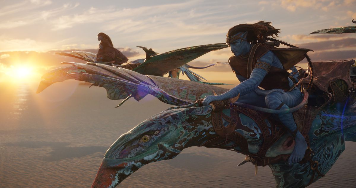Los compañeros de Na'vi Neytiri (Zoe Saldaña) y Jake (Sam Worthington) vuelan en sus monturas banshee azules moteadas sobre las nubes con una puesta de sol detrás de ellos en Avatar: The Way of Water