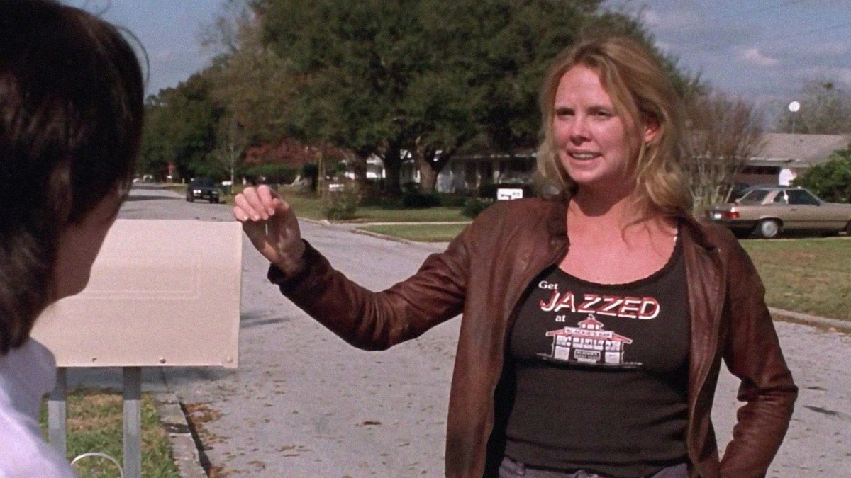 Canavar filminde Charlize Theron, biriyle konuşurken elini bir posta kutusuna koyuyor. Üzerinde bir kurum resmi olan “JAZZED at” yazan bir gömlek giyiyor.