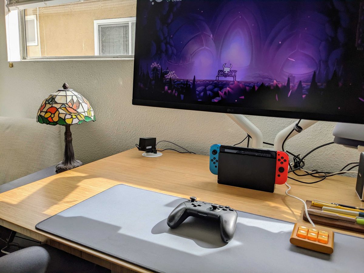 A desk setup with a Nintendo Switch and a large gaming monitor, with a Nintendo Switch pro controller on a desk mat.