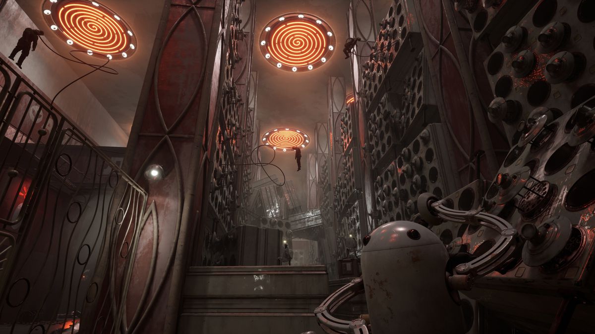 A high-ceilinged, dark facility, lit by red spirals on the ceiling, with racks of cylindrical canisters and human figures dangling high up from long tendrils