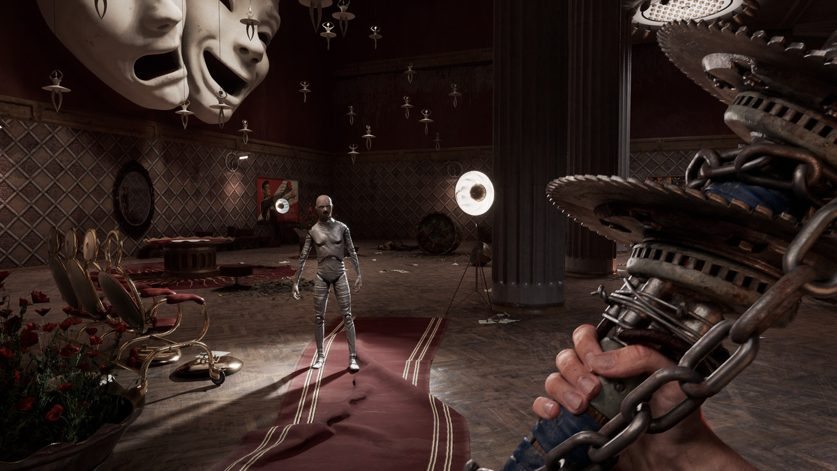 An android approaches in a large room with theatrical masks on the wall and tiny ballerina figures hanging from the ceiling. In the foreground, the first-person view shows a hand holding a heavy bladed weapon