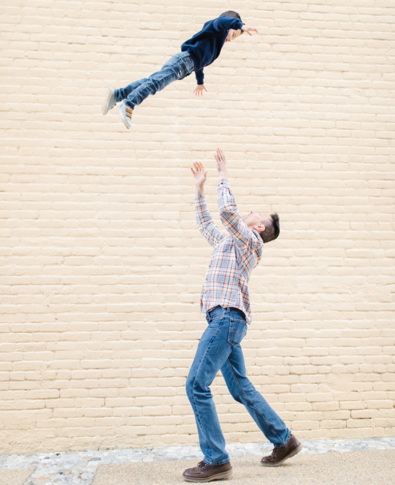 Père jouant avec son enfant devant un mur de briques