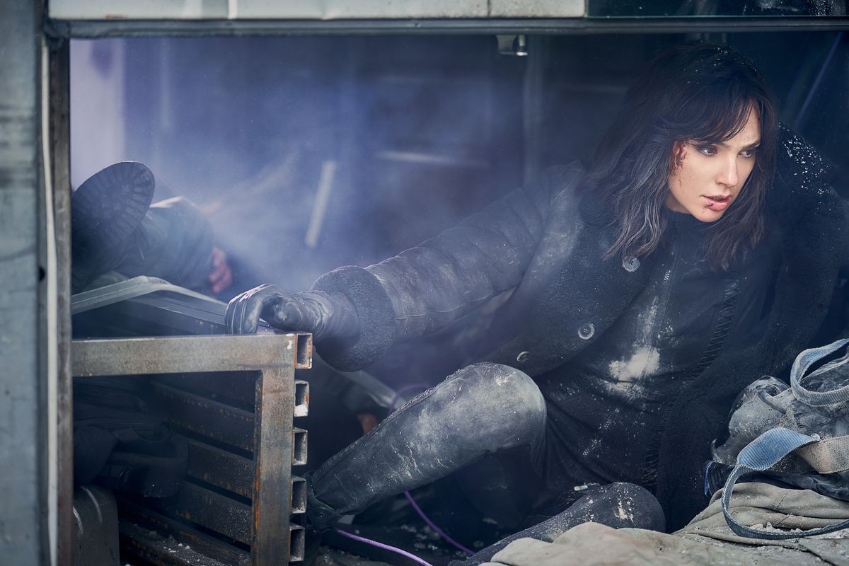 a dark haired woman looking disheveled, but still effortlessly cool as she hides among some construction equipment