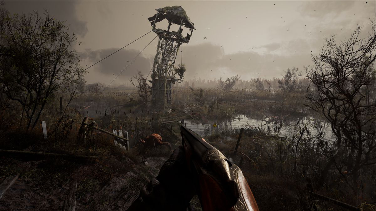 A first-person view in STALKER 2, with the player aiming a shotgun in the direction of a decrepit lookout tower. A small lake and a mutated monster are nearby.