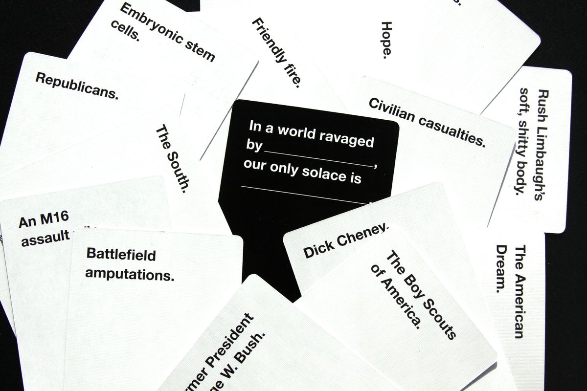 Karten gegen die Menschlichkeitskarten, die auf einem Tisch liegen. Auf der schwarzen Karte steht: „In einer Welt, die von (Leerzeichen) verwüstet wird, ist unser einziger Trost (Leerzeichen.)