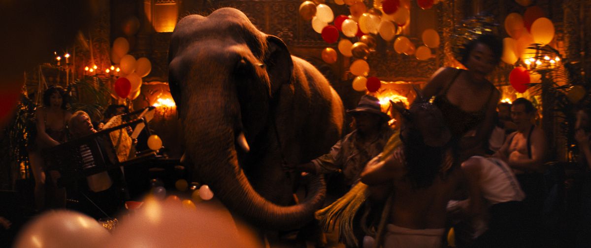 يخطو فيل عبر أرضية قاعة مضاءة بضوء أحمر خافت ، ويدفع من خلال رواد الحفلات والبالونات في بابل