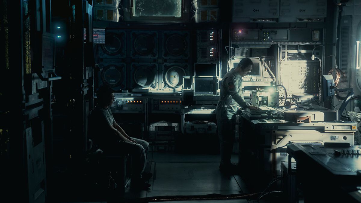 Een man buigt zich over een tafel om naar iets te kijken in een donker, futuristisch ogend wetenschappelijk laboratorium in The Wandering Earth II
