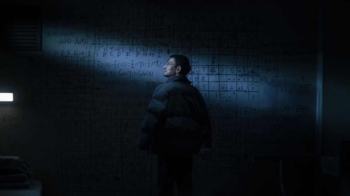 The Wandering Earth II'de bir adam, karanlık, soğuk görünen bir odada, matematiksel semboller ve formüllerle kaplı, tek bir ışık huzmesiyle loş bir şekilde aydınlatılmış devasa bir karatahtanın önünde duruyor.