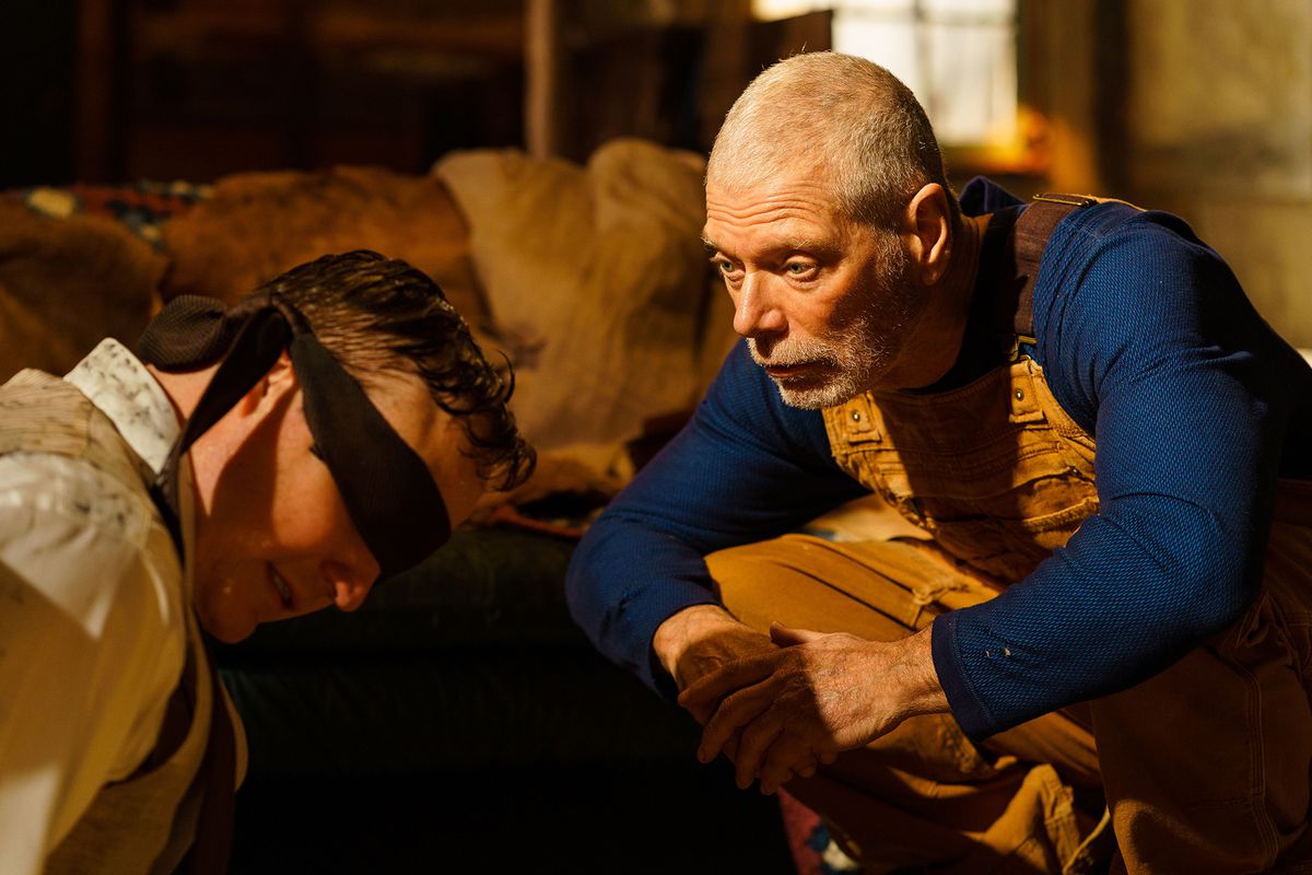 Uzun kollu mavi gömlekli ve sarı tulumlu yaşlı bir adam (Stephen Lang), gözleri bağlı bir adamın (Marc Senter) önünde çömelir.