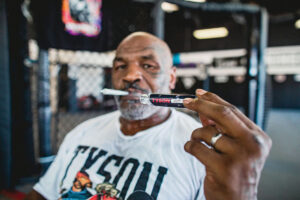 Mike Tyson con un porro preliado en la boca sosteniendo el tubo preliado en el primer plano de la imagen