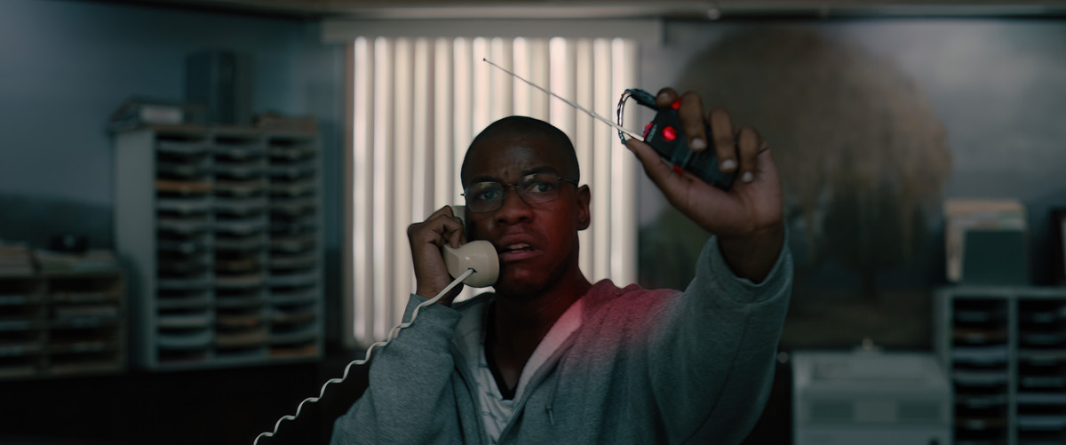 Breaking에서 John Boyega는 회색 후드티를 입고 한 손에는 기폭 장치를 들고 다른 한 손에는 전화를 합니다.