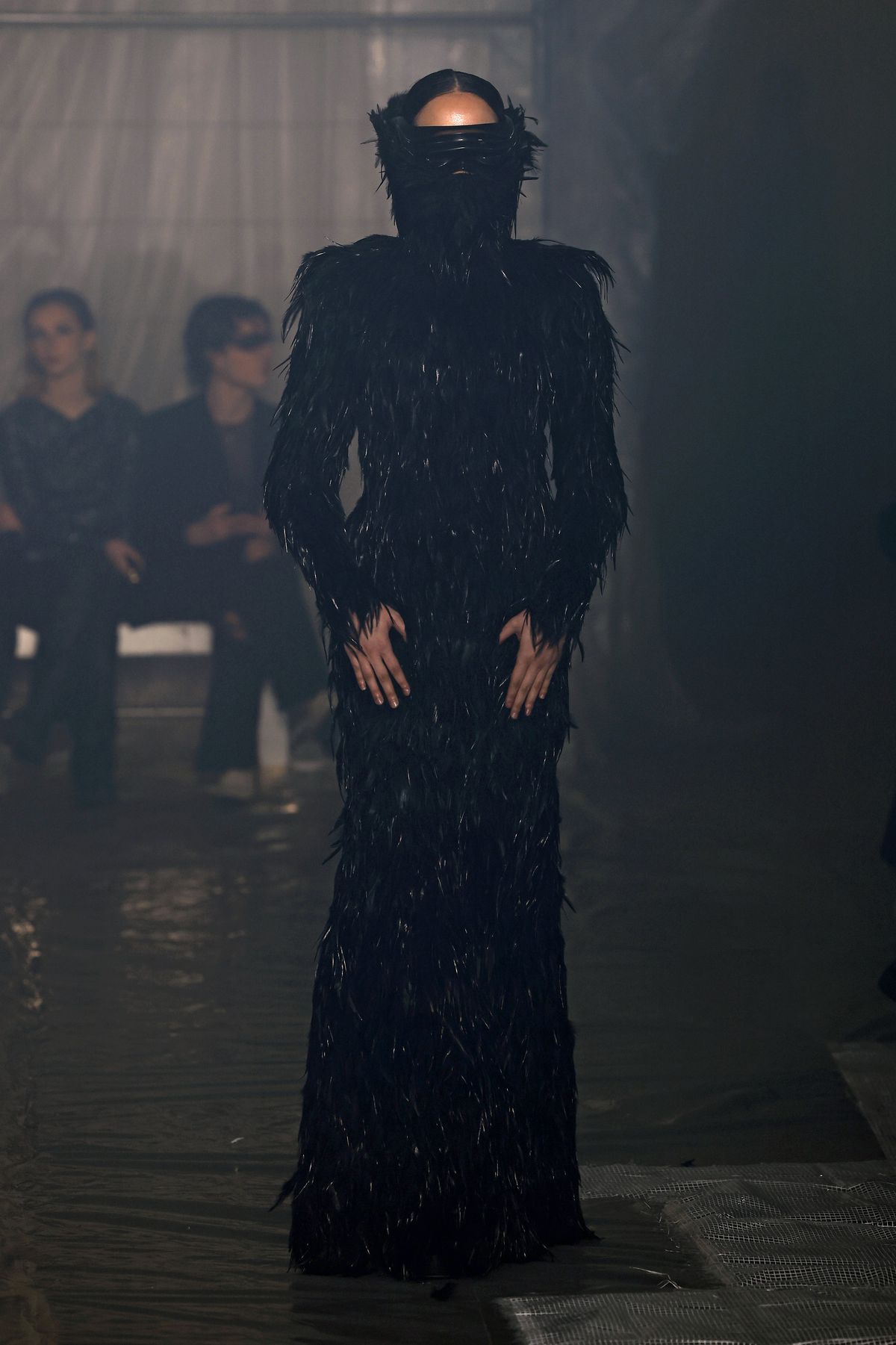 A model wearing a long black feathered dress and face-obscuring sunglasses walks the runway at the Han Kjobenhavn fashion show at Milan Fashion Week.