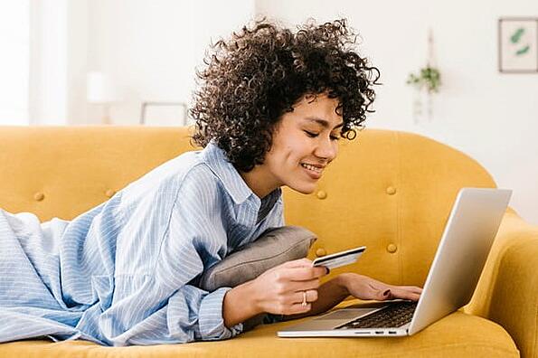 A woman holding a credit card is on her laptop and looking at product attributions before making a purchase.