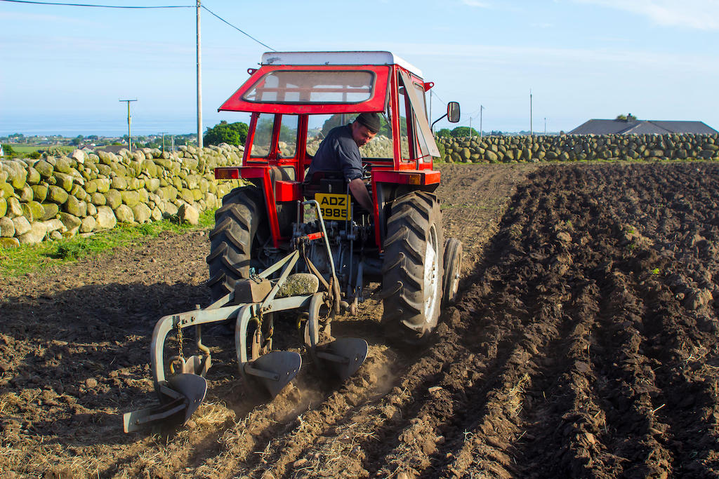 Een kleine tractor en ploeg van Massey Ferguson aan het werk in een veld nabij de Mountains of Mourne in Noord-Ierland, VK.