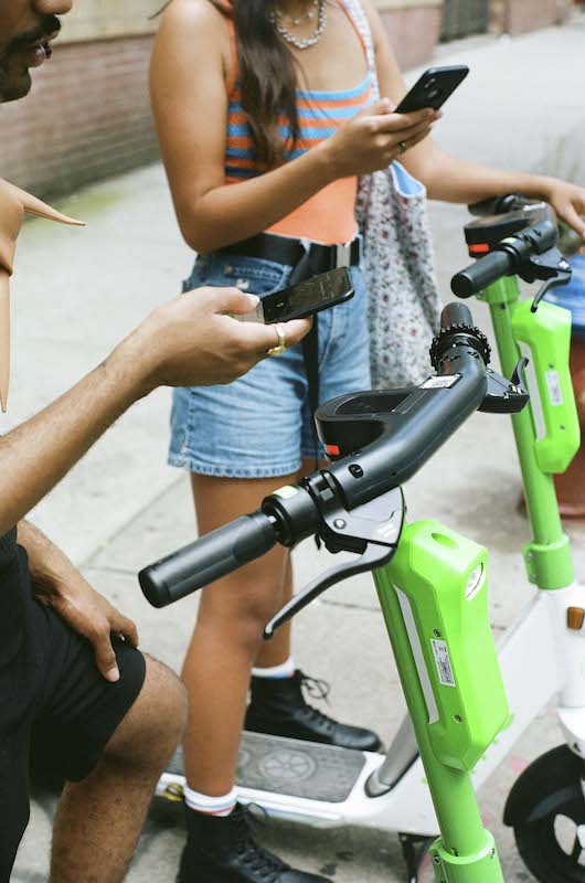 A woman and man standing near lime-green e-scooters