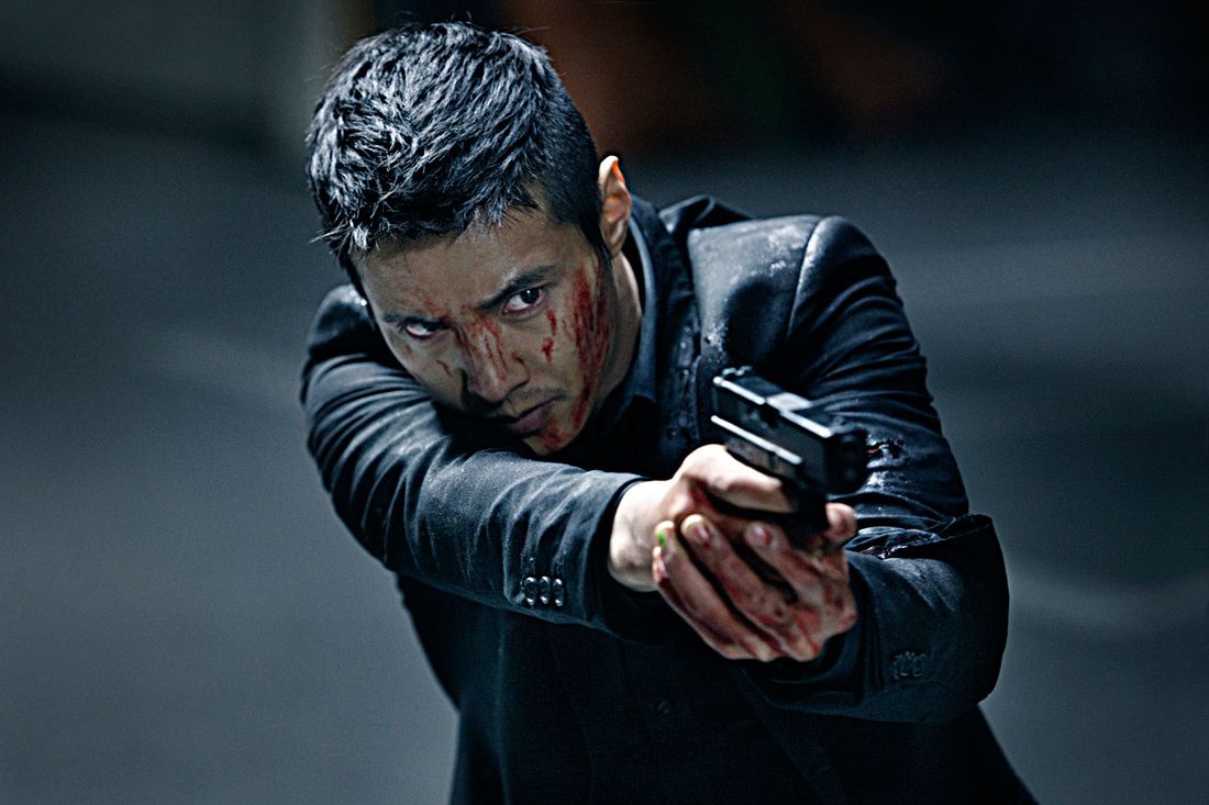 Un hombre con un traje negro (Won Bin) con sangre en la cara y las manos apunta con la mira de una pistola a un objetivo fuera de la pantalla.