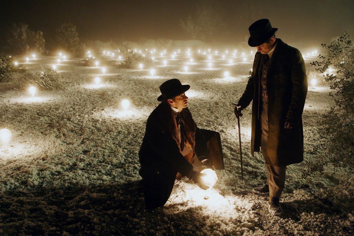 un hombre sostiene un orbe brillante en The Prestige, junto a otro hombre en la nieve
