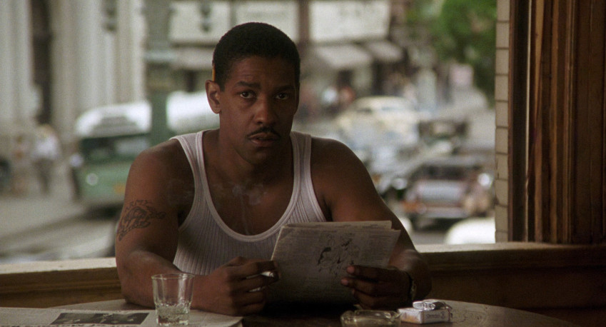 Denzel Washington, vestido con una camiseta sin mangas blanca, lee el periódico en Devil in a Blue Dress.