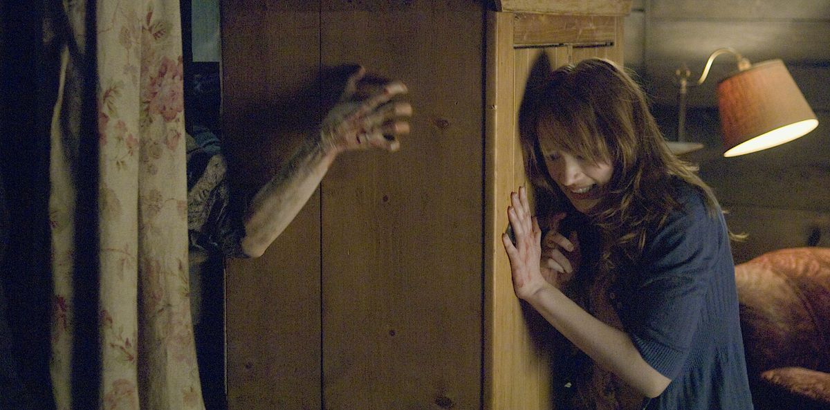 Dana (Kristen Connolly) pushes a tall wooden wardrobe up against a smashed window as zombies try to fight their way into her rustic cabin in 2011’s The Cabin in the Woods