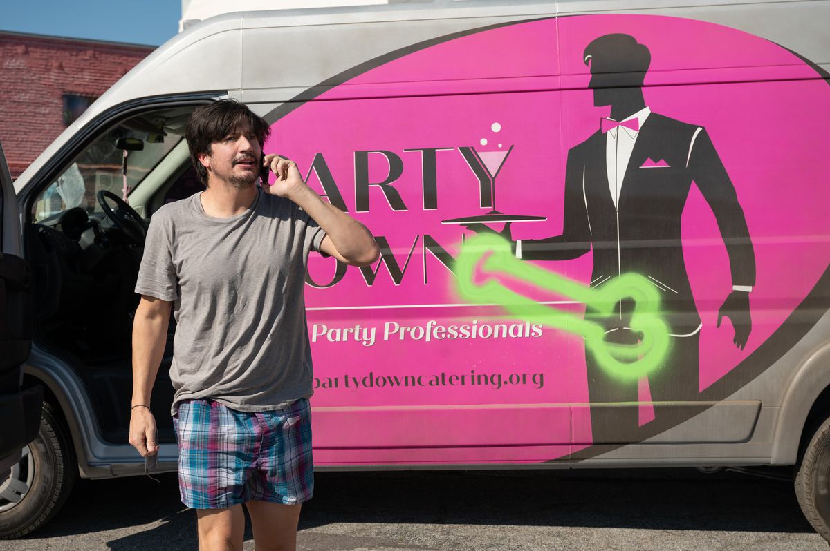 Ron Donald (Ken Marino) standing in front of the Party Down van looking disheveled in his boxers. The logo has a penis spray painted on it
