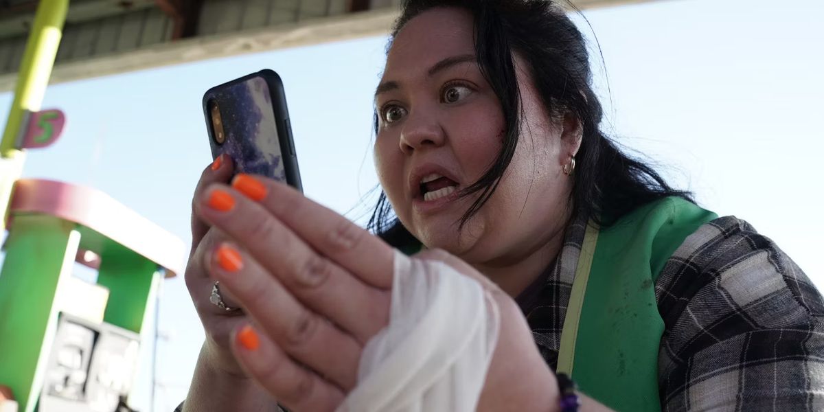 Μια γυναίκα (Jolene Purdy) κοιτάζει με αγωνία ένα κινητό τηλέφωνο με ένα δεμένο χέρι.