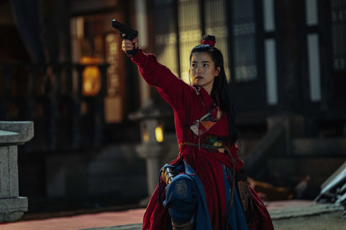 Μια γυναίκα (Kim Tae-ri) με τα μαλλιά της σε κότσο ντυμένη με κόκκινο και μπλε κιμονό στοχεύει ένα πιστόλι εκτός οθόνης ενώ είναι γονατισμένη στη μέση μιας αυλής.