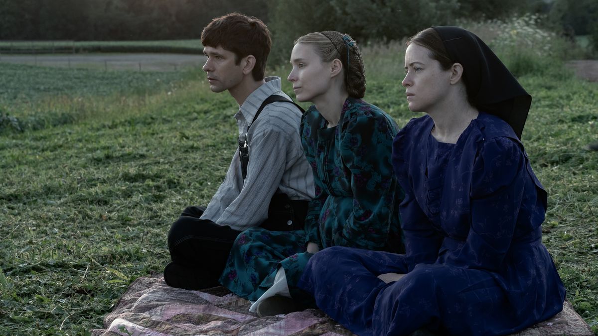 Ένας άντρας (Ben Whishaw), μια γυναίκα (Rooney Mara) και μια άλλη γυναίκα (Claire Foy) κάθονται σε μια κουβέρτα με θέα σε ένα χωράφι με πράσινο γρασίδι.