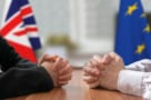 Bir AB bayrağı ve bir Birleşik Krallık bayrağı bulunan bir tahta masasında iki çift elin fotoğrafı