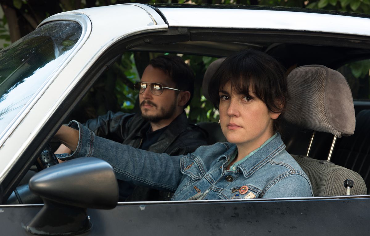 (L-R) Elijah Wood and Melanie Lynskey seated behind the wheel of a car in I Don’t Feel At Home in This World Anymore