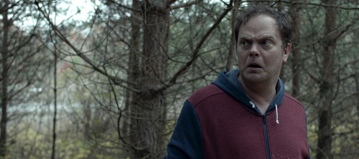 Rainn Wilson standing in a forest looking perplexed in 2017’s Shimmer Lake