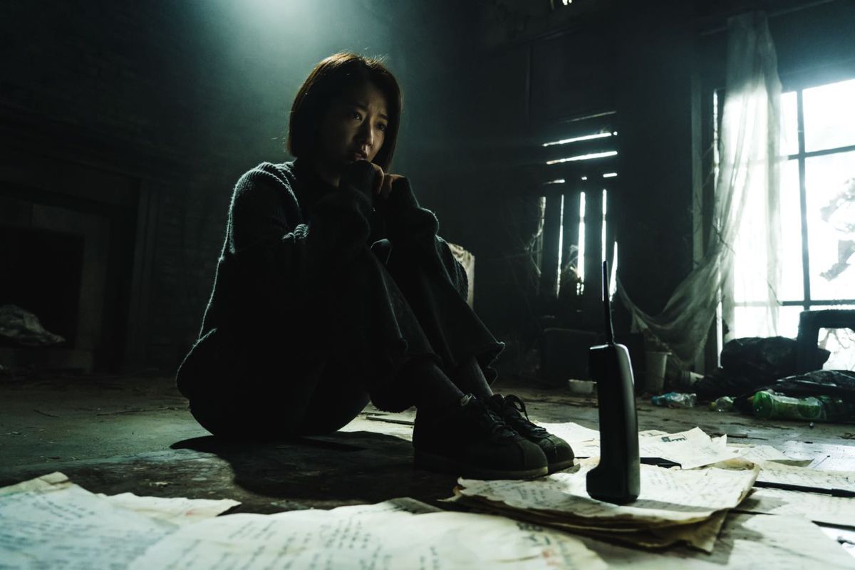 Park Shin-hye assis en face d'un téléphone domestique sans fil dans un salon sombre et délabré dans The Call (2020)