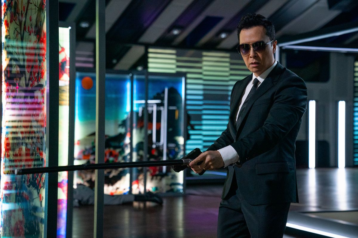 Донни Йен в костюме и солнцезащитных очках протягивает пистолет и банку в фильме «Джон Уик: Глава 4».