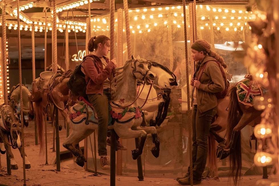 Ellie (Bella Ramsey) sentada en un caballo de carrusel y hablando con Riley (Storm Reid)